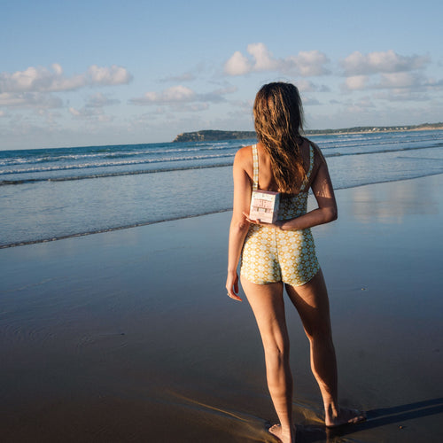 Woman standing on a beach holding a candle, facing the ocean.