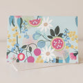 A greeting card with a blue background and a floral design featuring various flowers and fruit illustrations.